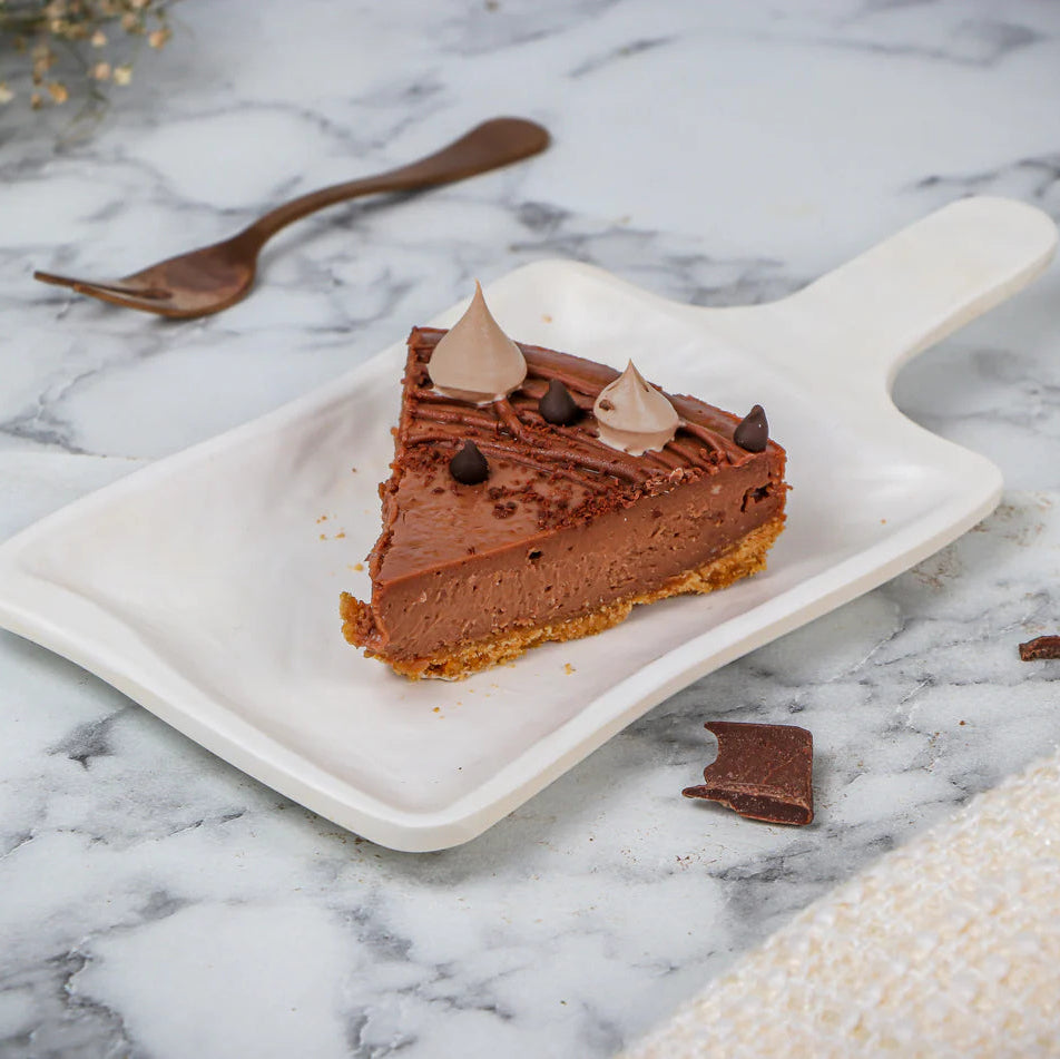 A single slice of chocolate cheesecake on a white plate with a fork beside it, placed on a marble surface.
