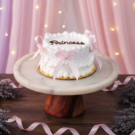 White cake with 'Princess' on a marble stand with pink ribbons against a soft pink curtain background for womens day.