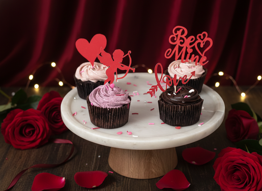 Cupcakes on a white marble stand with decorative toppers and red roses on a dark background