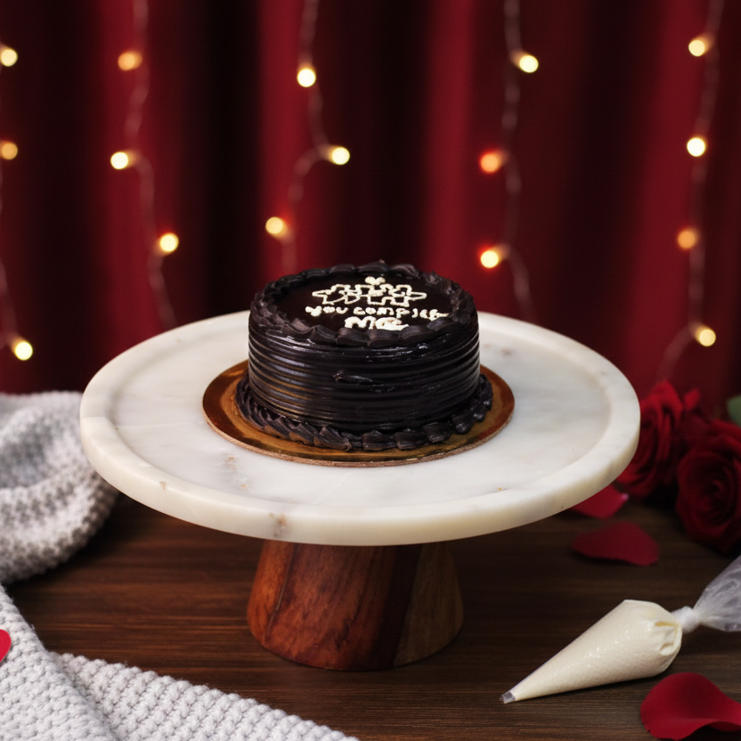 Chocolate cake on a marble stand with red roses and decorative elements against a warm, blurred background.